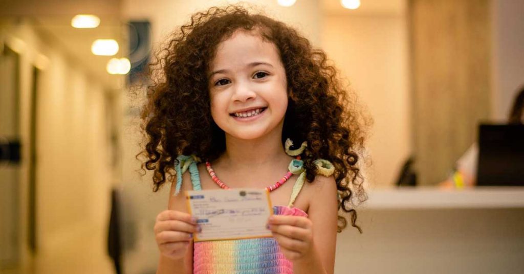 Criança sorrindo segurando a carteira de vacinação infantil em ambiente de saúde